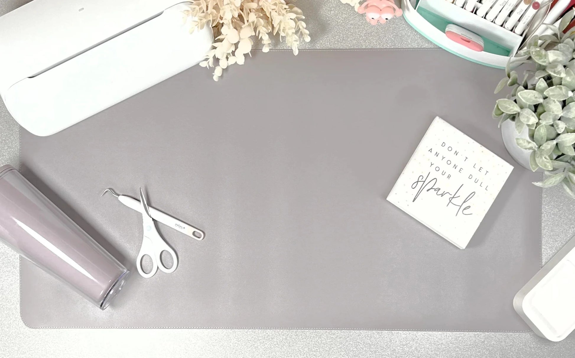 Gray desk mat with scissors, roll of paper, and decorative items on a light surface.