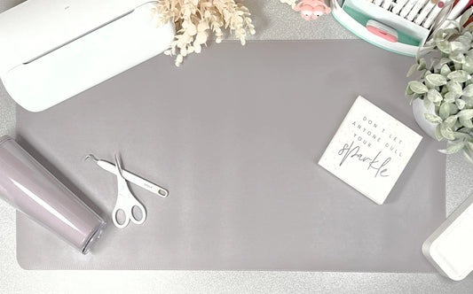 Gray desk mat with scissors, roll of paper, and decorative items on a light surface.