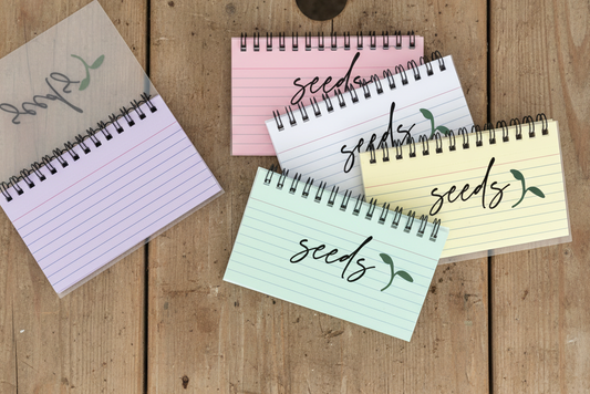 Five small spiral-bound notebooks with 'seeds' text on a wood surface
